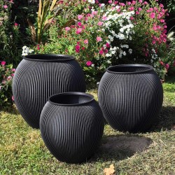 trois gros pots de fleurs gris anthracite de taille differente dans un jardin